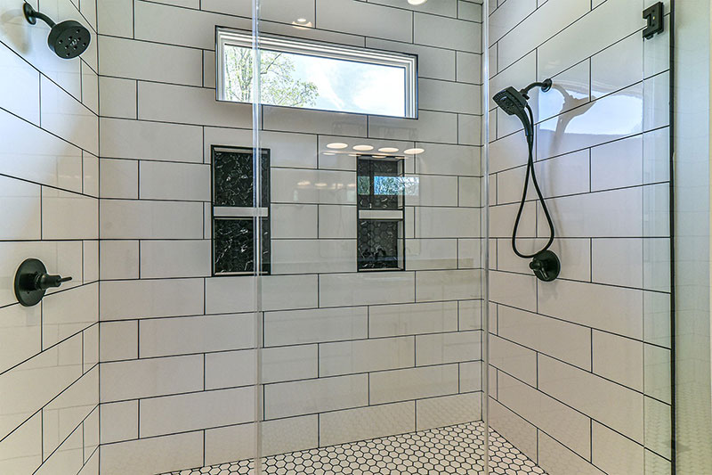 Walk-in shower with white subway tile, two shower heads, tiled niches and a glass partition