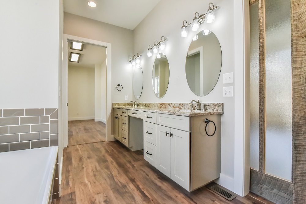 Primary bath with a double vanity, oval mirrors and a tiled tub surround