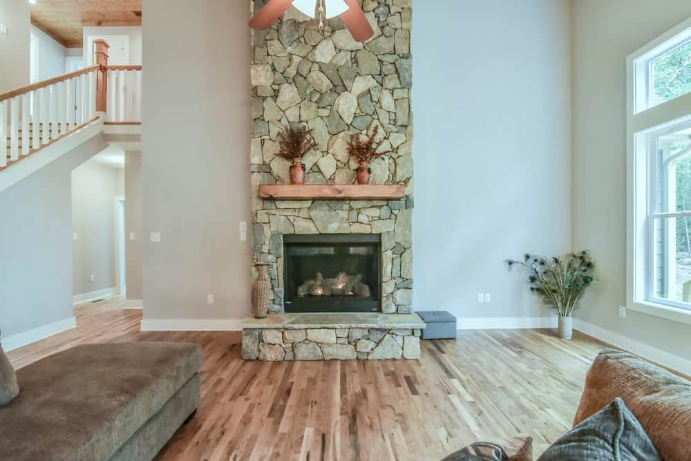 Two-story living room with a stone fireplace, wood mantel and an open stair landing above