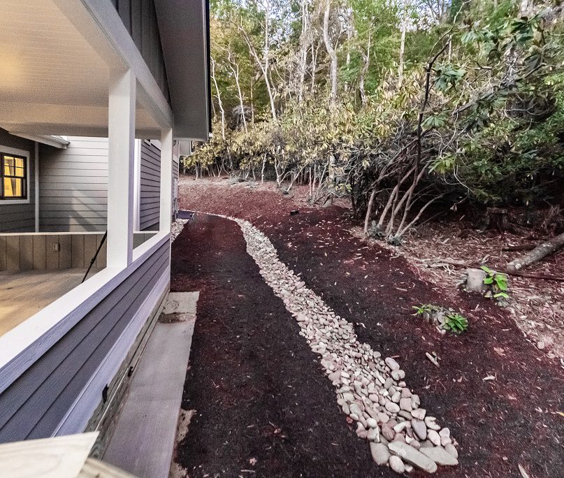 Side yard with a river-rock drainage bed and fresh landscaping along the house