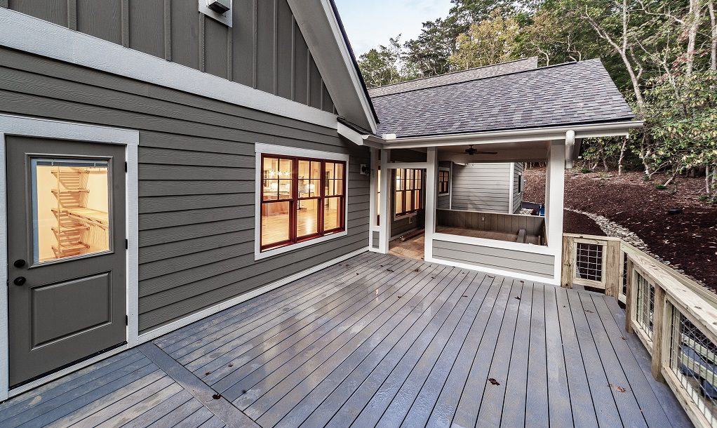 Covered rear deck with gray siding, a wood railing and a screened section