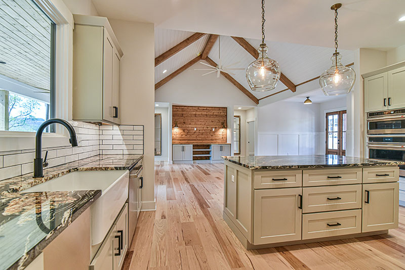 Kitchen sink with a black faucet, granite counters and a view across the island to the great room