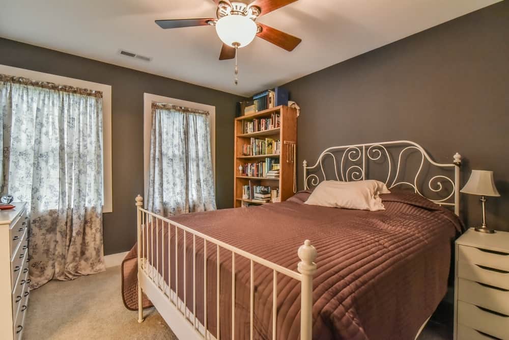 Bedroom with a gray accent wall, bookshelves and curtained windows