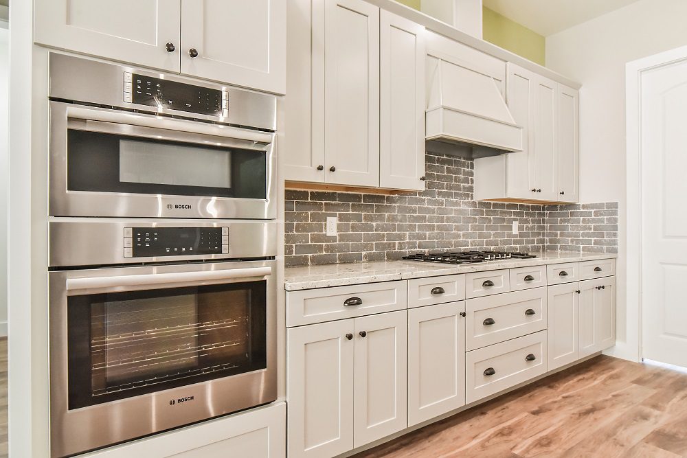 Kitchen with white cabinets, double wall ovens, a gas cooktop and a gray tile backsplash