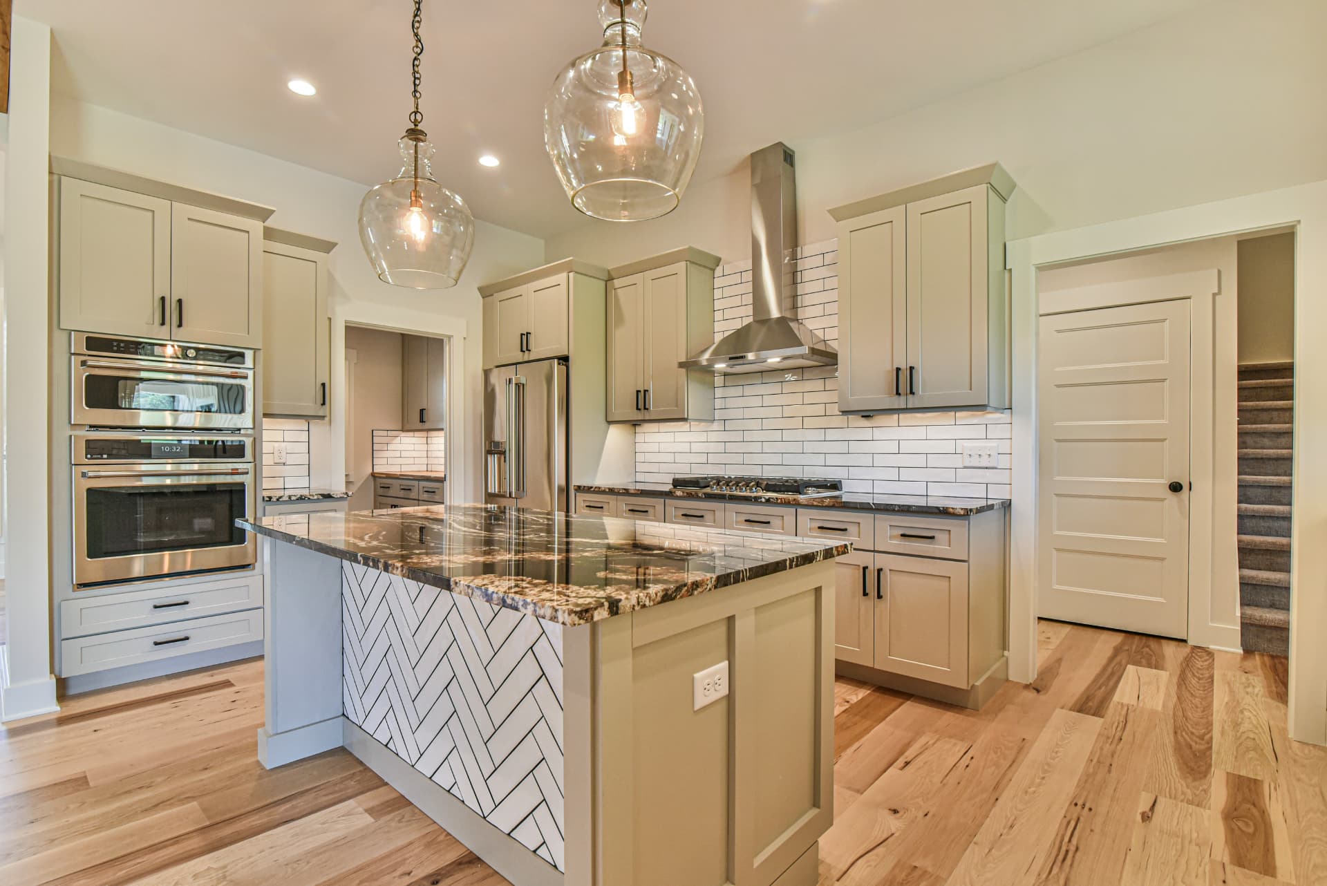 Upscale custom kitchen with herringbone island, granite counters, glass pendants, and painted cabinetry