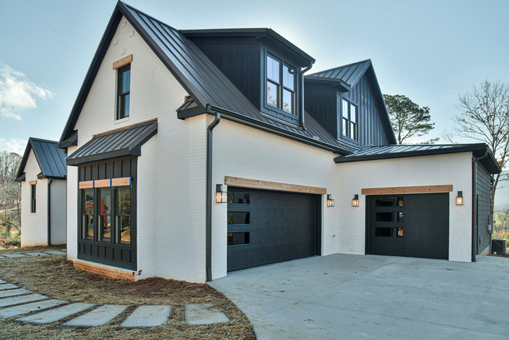 Front and side view of the white farmhouse with black garage doors and a covered entry