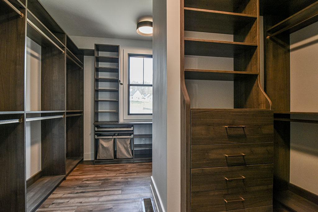 Walk-in closet with dark wood shelving, drawers and a window