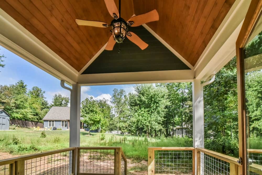 Covered porch with a vaulted stained-wood ceiling, ceiling fan and wire railing