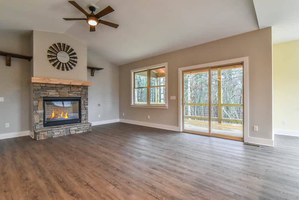 Living room with a stone fireplace, vaulted ceiling, ceiling fan and sliding doors to the deck