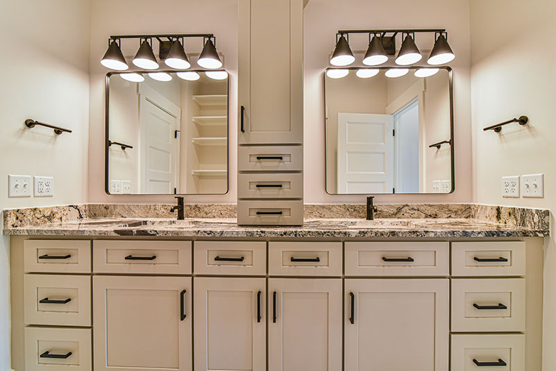 Primary bath with a long double vanity, granite counters, two mirrors and built-in storage