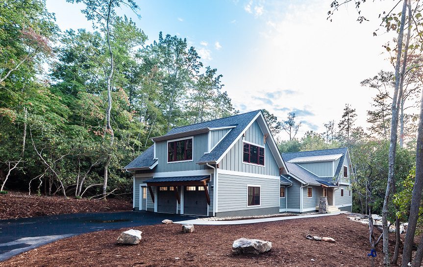 Side view of the gray mountain home with gabled roofs and a wooded driveway