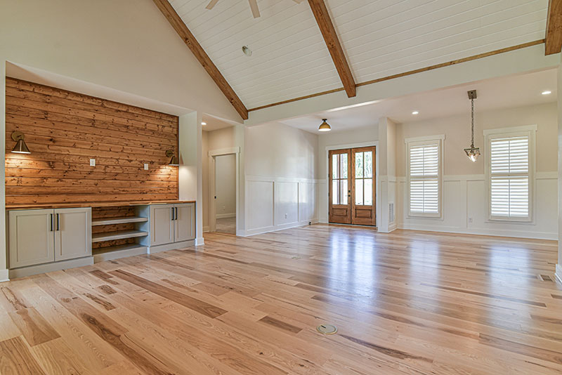 Great room with a vaulted ceiling, exposed wood beams, wood-plank accent wall and hickory floors