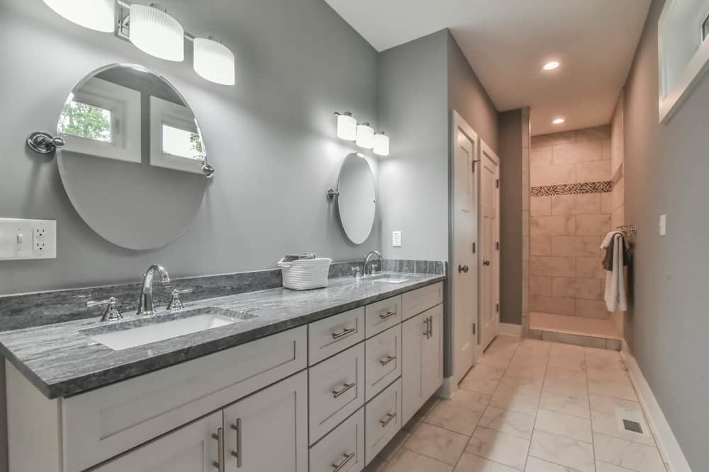 Primary bath with a long double vanity, round mirrors and a tiled walk-in shower