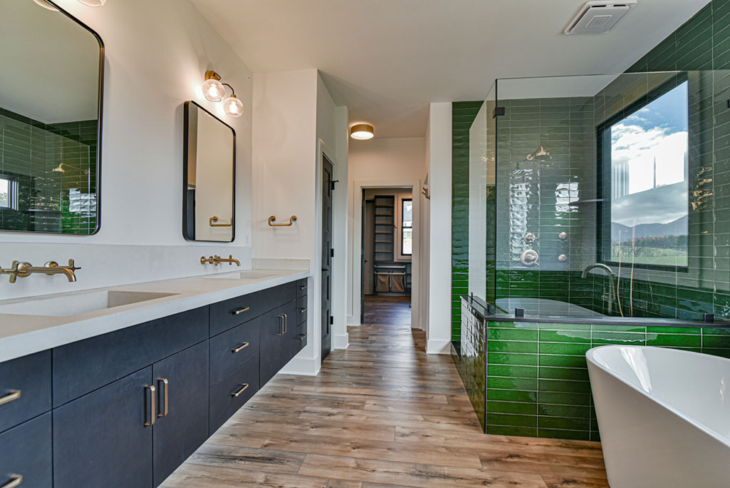 Primary bath with a long double vanity, freestanding tub and green-tiled walk-in shower