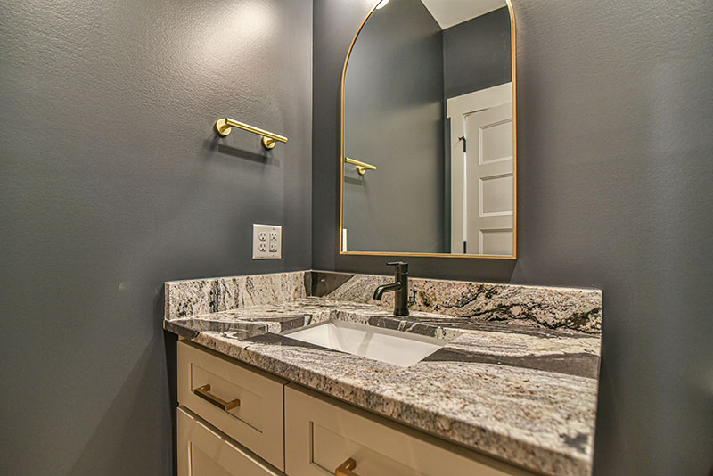 Powder room with a granite vanity, dark walls and a brass-framed mirror