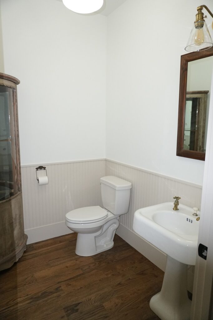 Powder room with a pedestal sink, beadboard wainscot and an antique-framed mirror