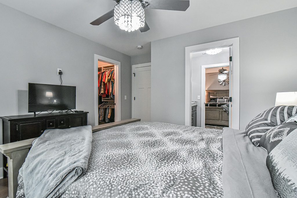 Bedroom with a walk-in closet, a doorway to the bath and a wall-mounted television