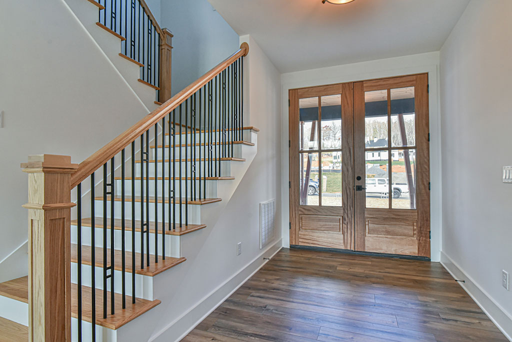 Entry foyer with glass double doors, wood stair treads and a black metal railing
