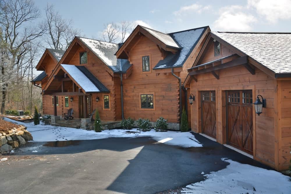 Timber and stone mountain home with shingled gables and a two-car garage in winter