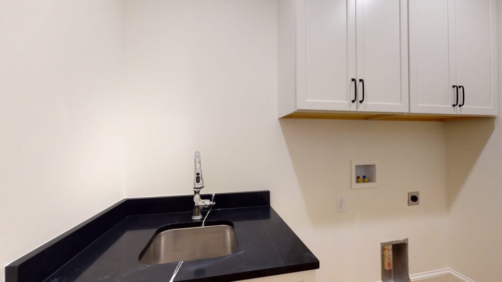 Laundry room with a black granite counter, undermount sink and white upper cabinets