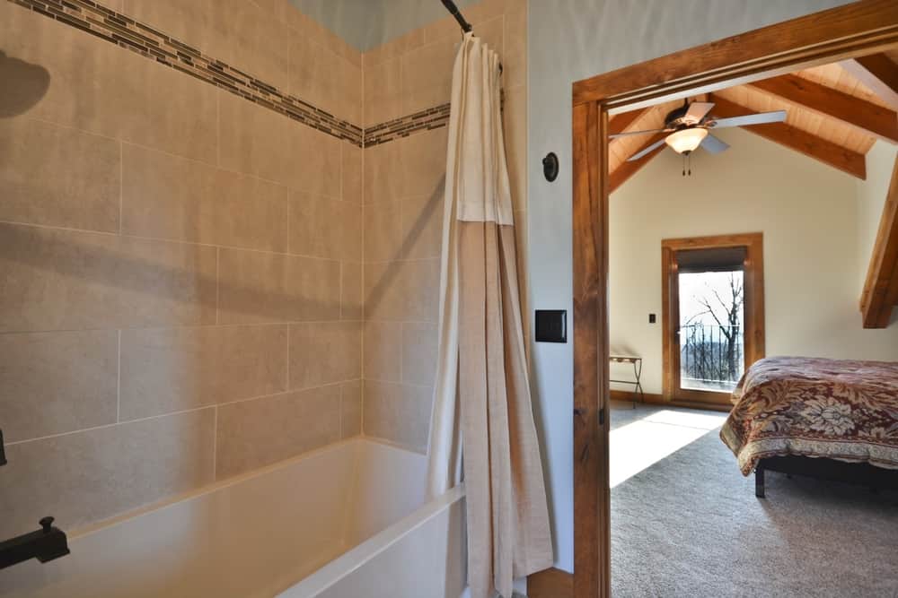 Guest bath with a tiled tub surround and a view into a bedroom with a vaulted ceiling