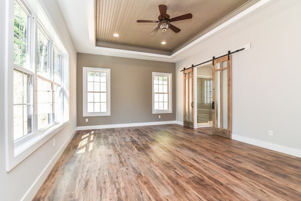 Primary bedroom with a tray ceiling, ceiling fan, windows and sliding barn doors