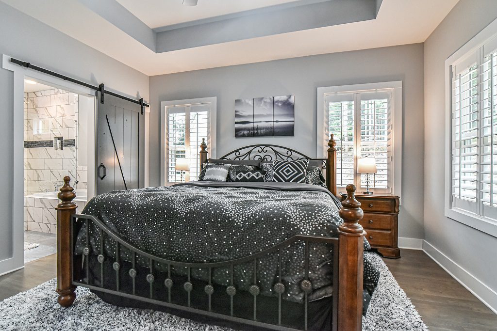 Primary bedroom with a tray ceiling, a barn door to the bath and plantation shutters