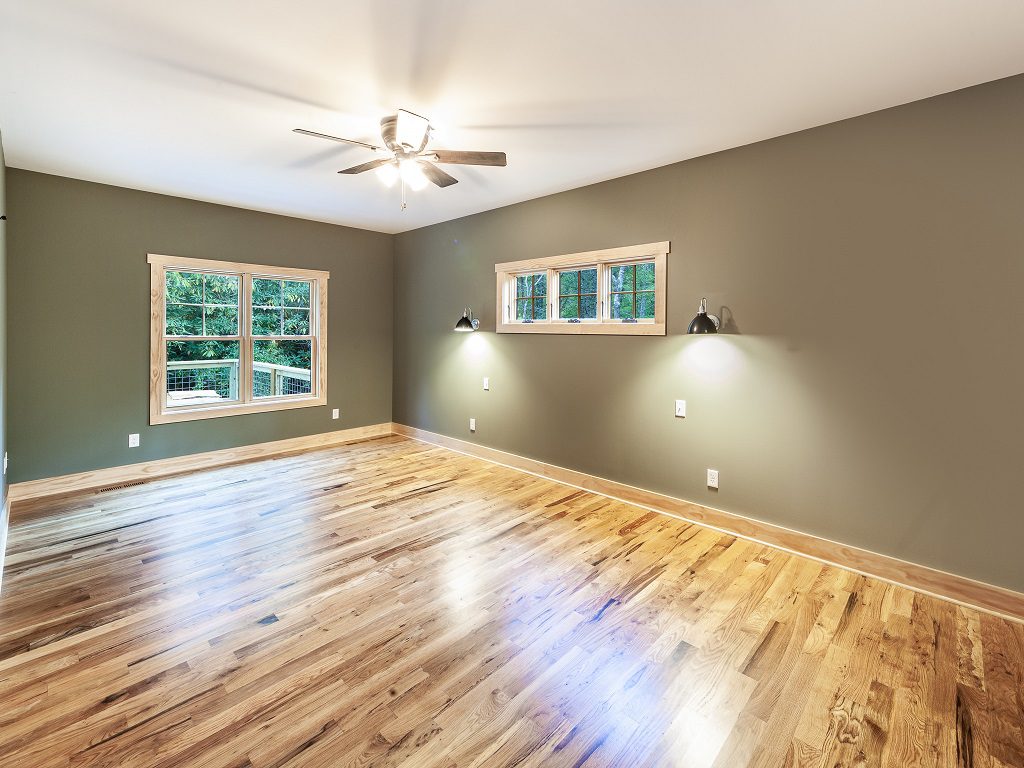 Primary bedroom with sage walls, hickory floors and barn-style wall sconces