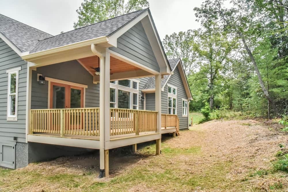 Side view of the home with a covered porch, wood railing and stained porch ceiling