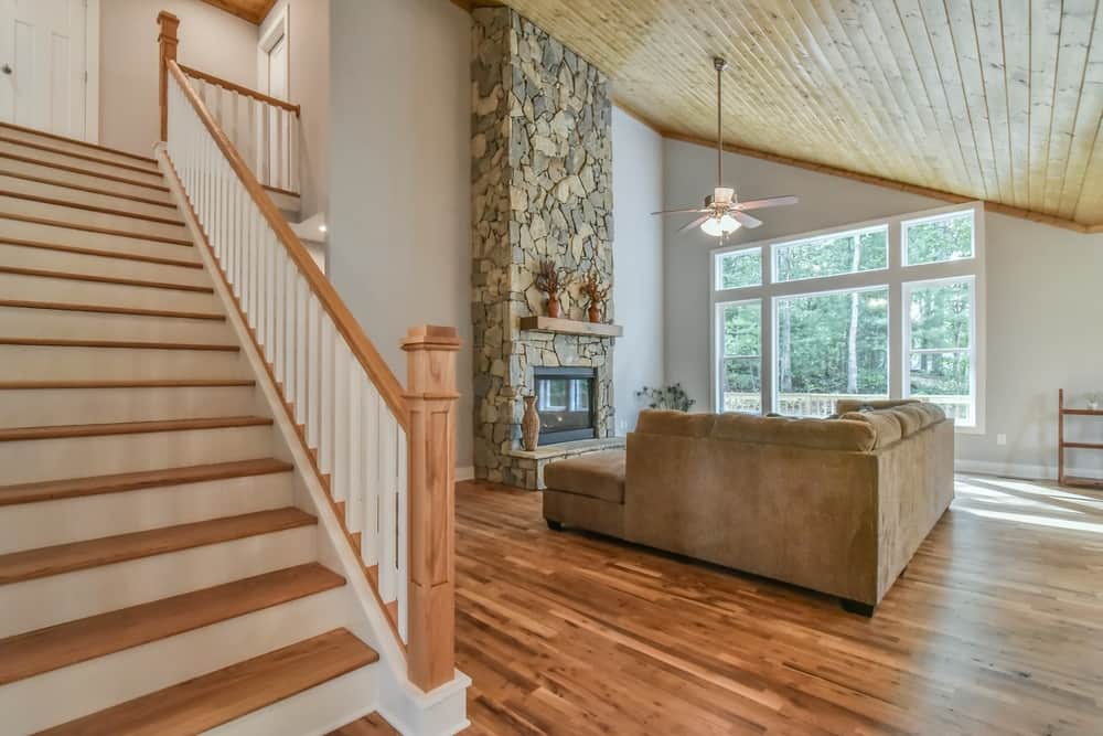 Stairway with wood treads and white risers beside a stone chimney and the living room