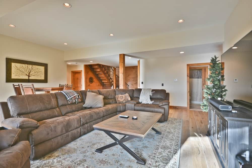 Lower-level family room with a sectional sofa, timber post and log-railed stairway