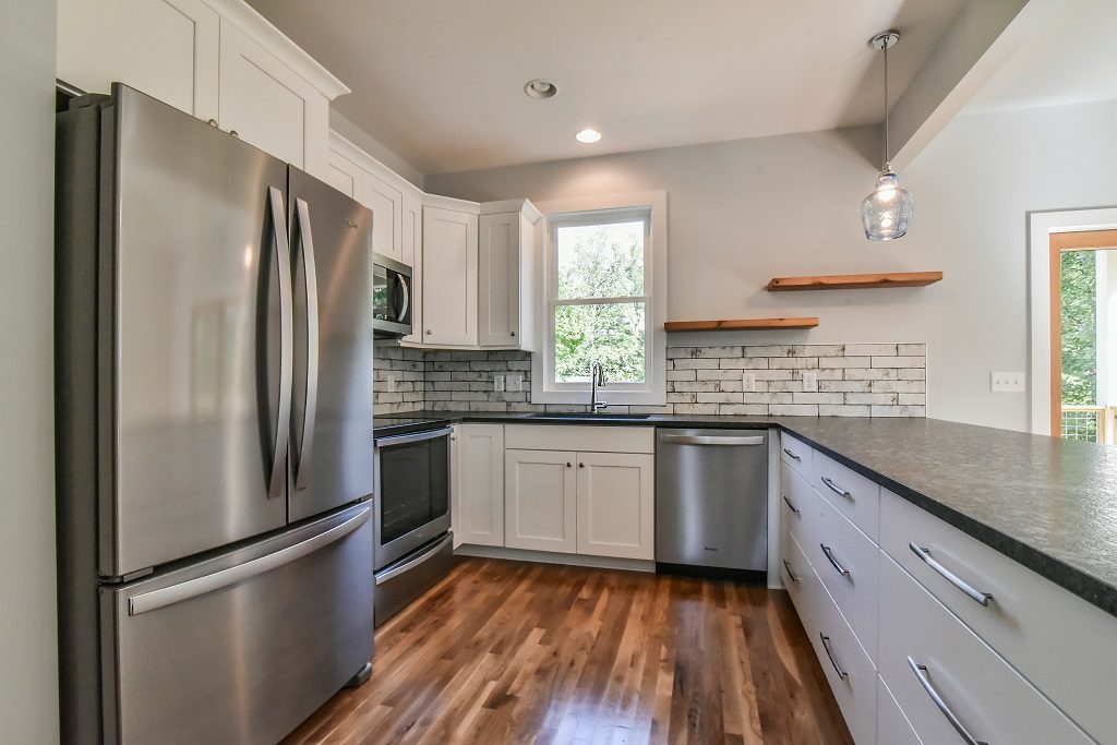 Kitchen with white cabinets, dark counters, a subway tile backsplash and stainless appliances