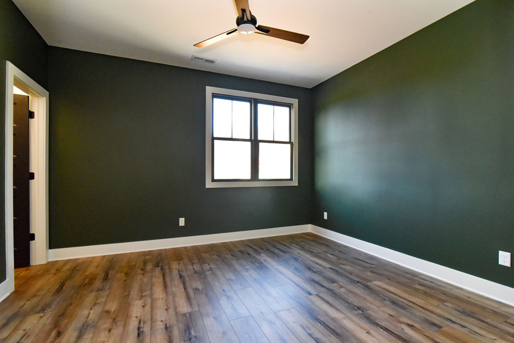 Bedroom with a deep green accent wall, ceiling fan and wood-look flooring