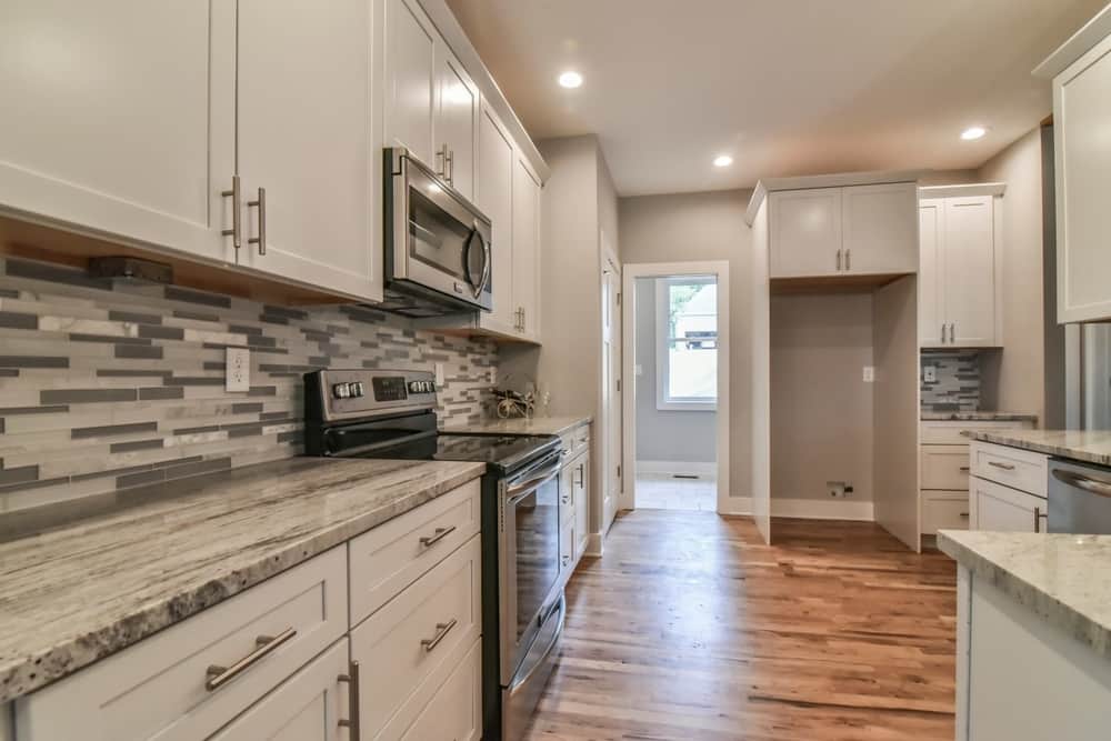 Kitchen with white cabinets, a tile backsplash, stainless range and a walk-through pantry