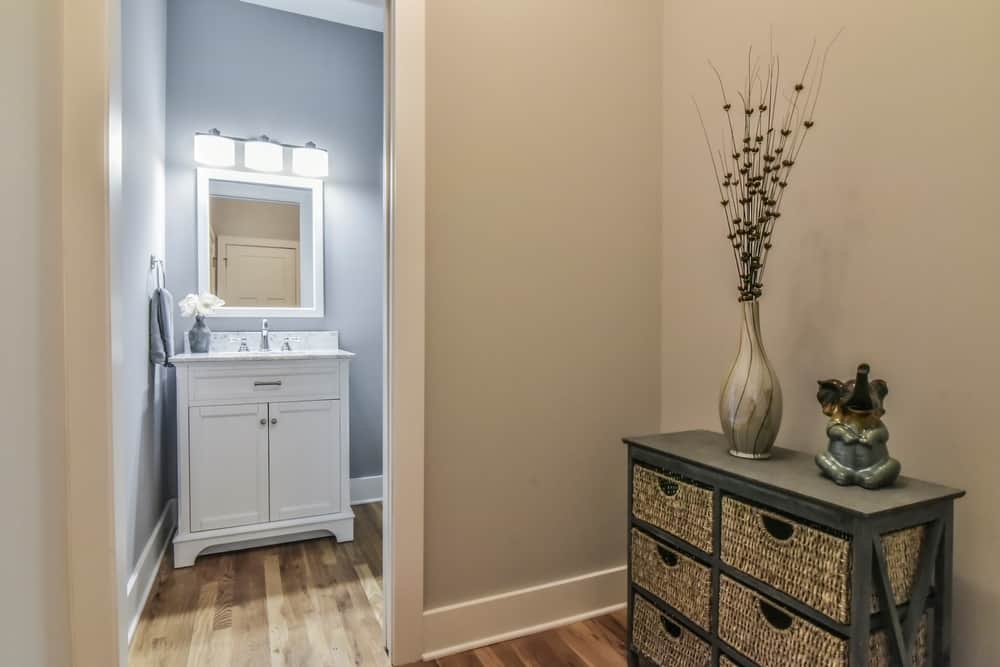 Powder room off the hallway with a white vanity, framed mirror and wood floors