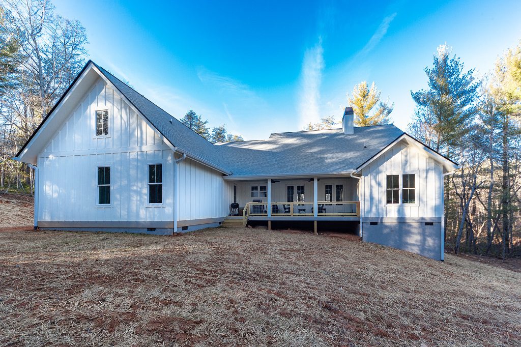 Rear view of the white farmhouse with a covered porch and brick chimney