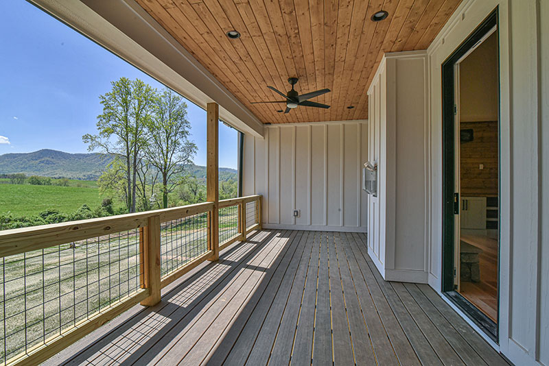 Covered porch with a stained wood ceiling, wire railing and a long pasture and mountain view