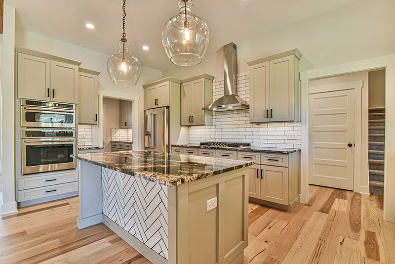 Kitchen with cream cabinets, a granite island with herringbone detail, wall ovens and glass pendant lights