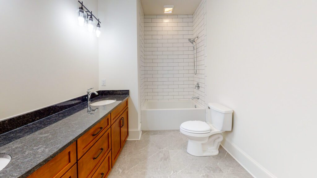 Bathroom with a tub and subway-tile surround, a dark wood vanity and stone counter
