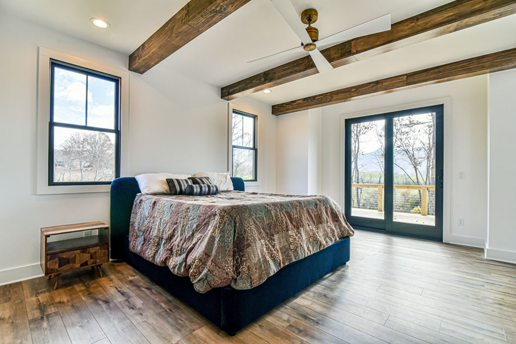 Primary bedroom with a beamed ceiling, large windows and doors to the deck