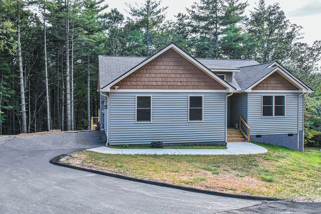 Front elevation of the gray home with a curved driveway and surrounding pines
