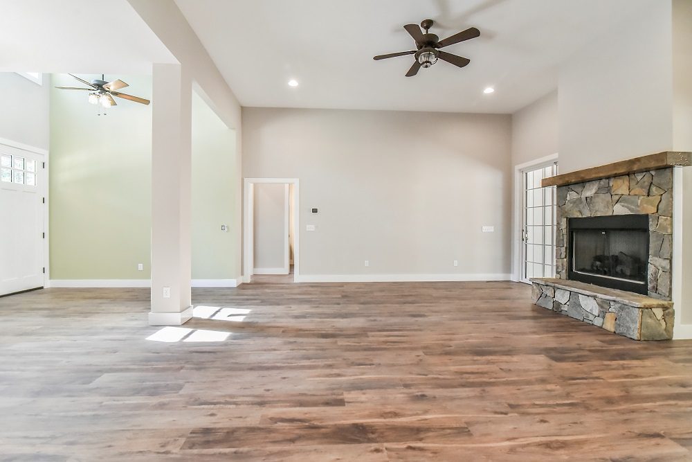 Living area with a stone fireplace, wood-look floors and a hallway beyond