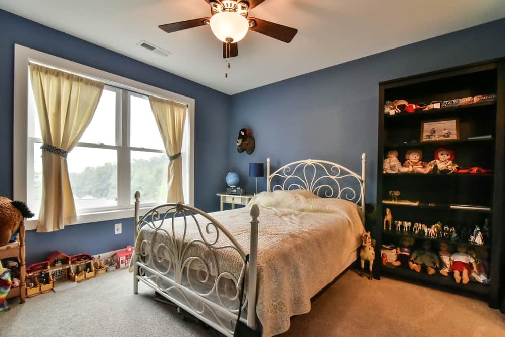 Bedroom with a blue accent wall, built-in bookshelves and a large window