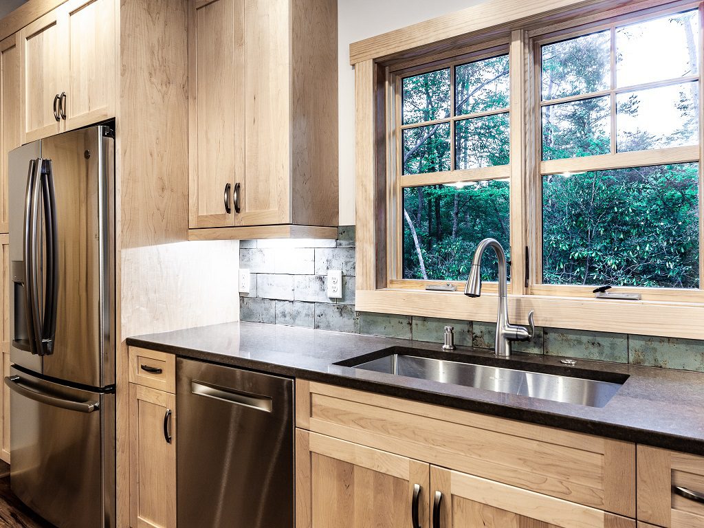 Kitchen with rustic wood cabinets, dark counters, stainless appliances and a window over the sink