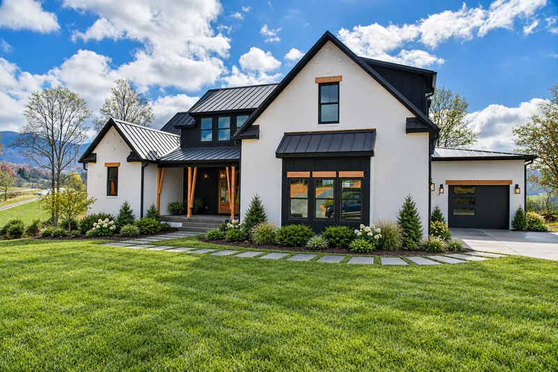 White modern farmhouse with black metal roof, landscaping, and mountain views