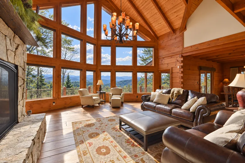 Great room interior with vaulted wood ceiling, stone fireplace, and wall of windows framing mountain views